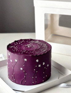 A purple cake sits atop a white box, surrounded by another white box, creating a simple yet elegant presentation.