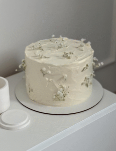 A white cake adorned with colorful flowers on top, elegantly presented for a special occasion.<br />
